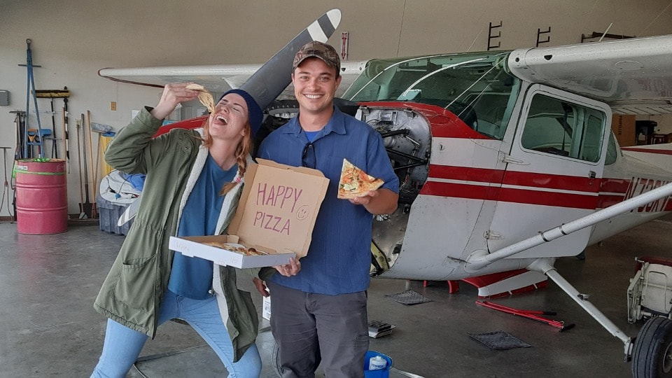 Students celebrating with pizza in front of ProFlite aircraft in hangar