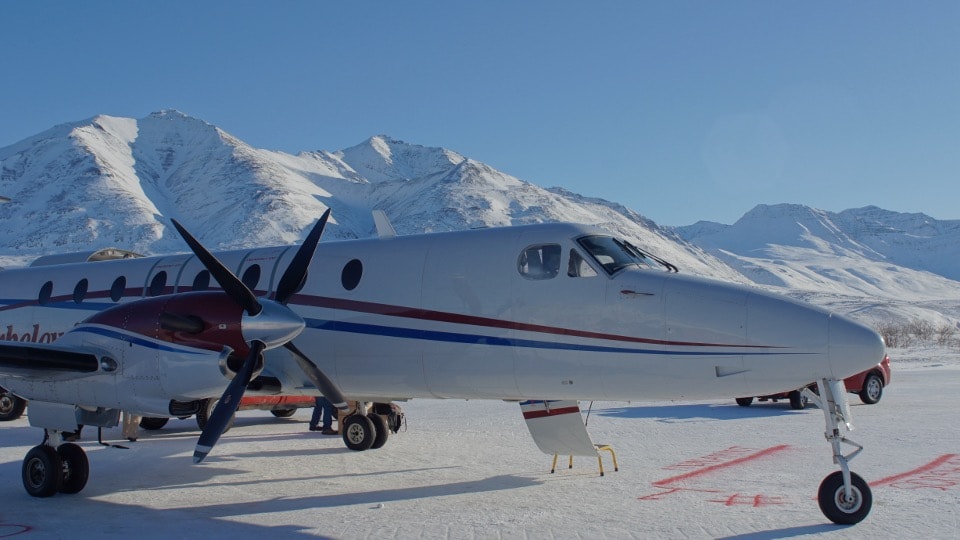 Turboprop aircraft on snowy Alaska ramp with mountains in background
