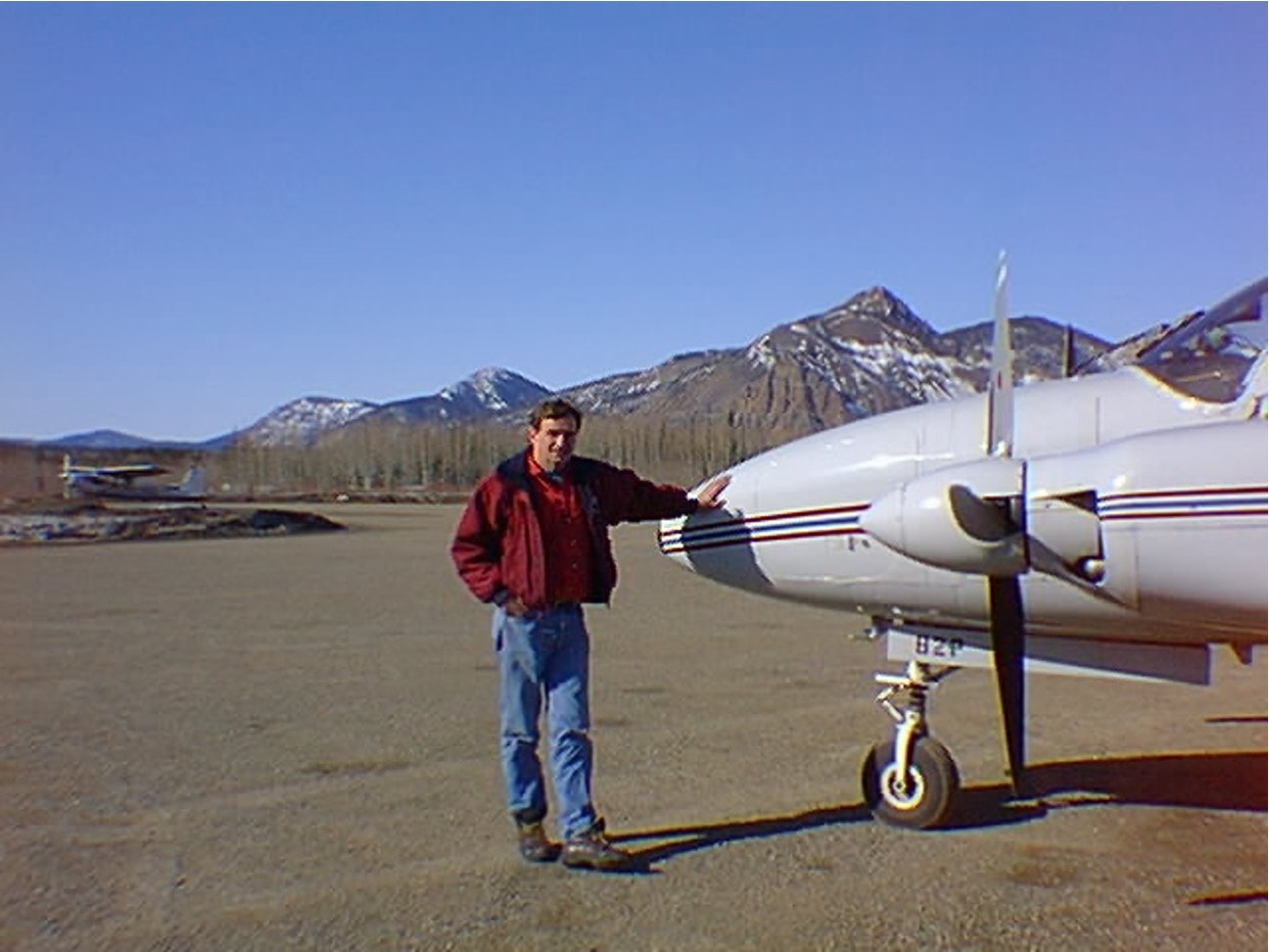 Pilot posing next to a twin-engine aircraft at Eagle, Alaska with mountains in the background