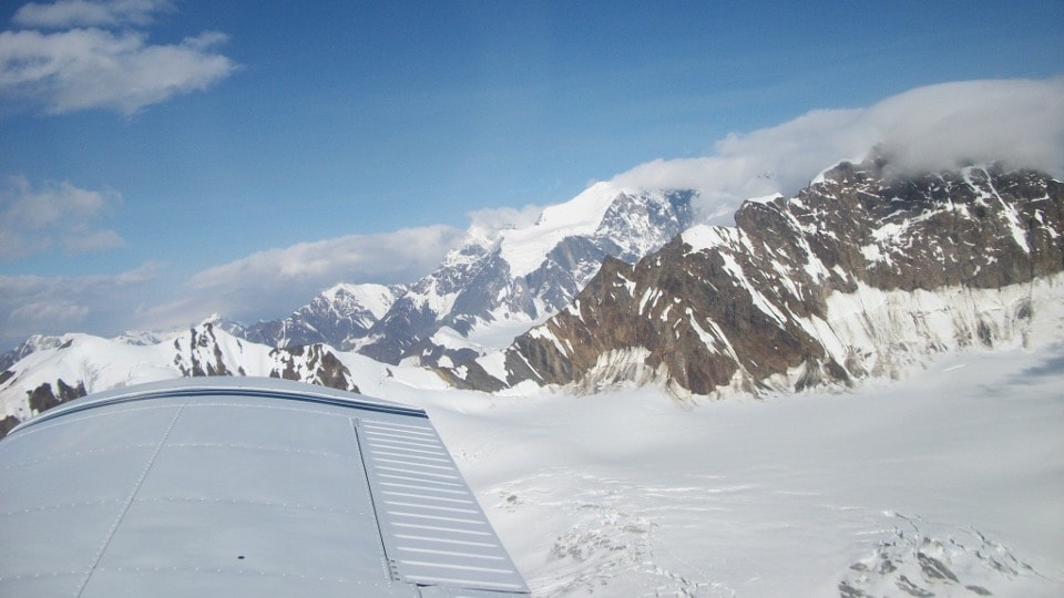 View from cockpit over aircraft wing toward the snow-covered Alaska Range peaks