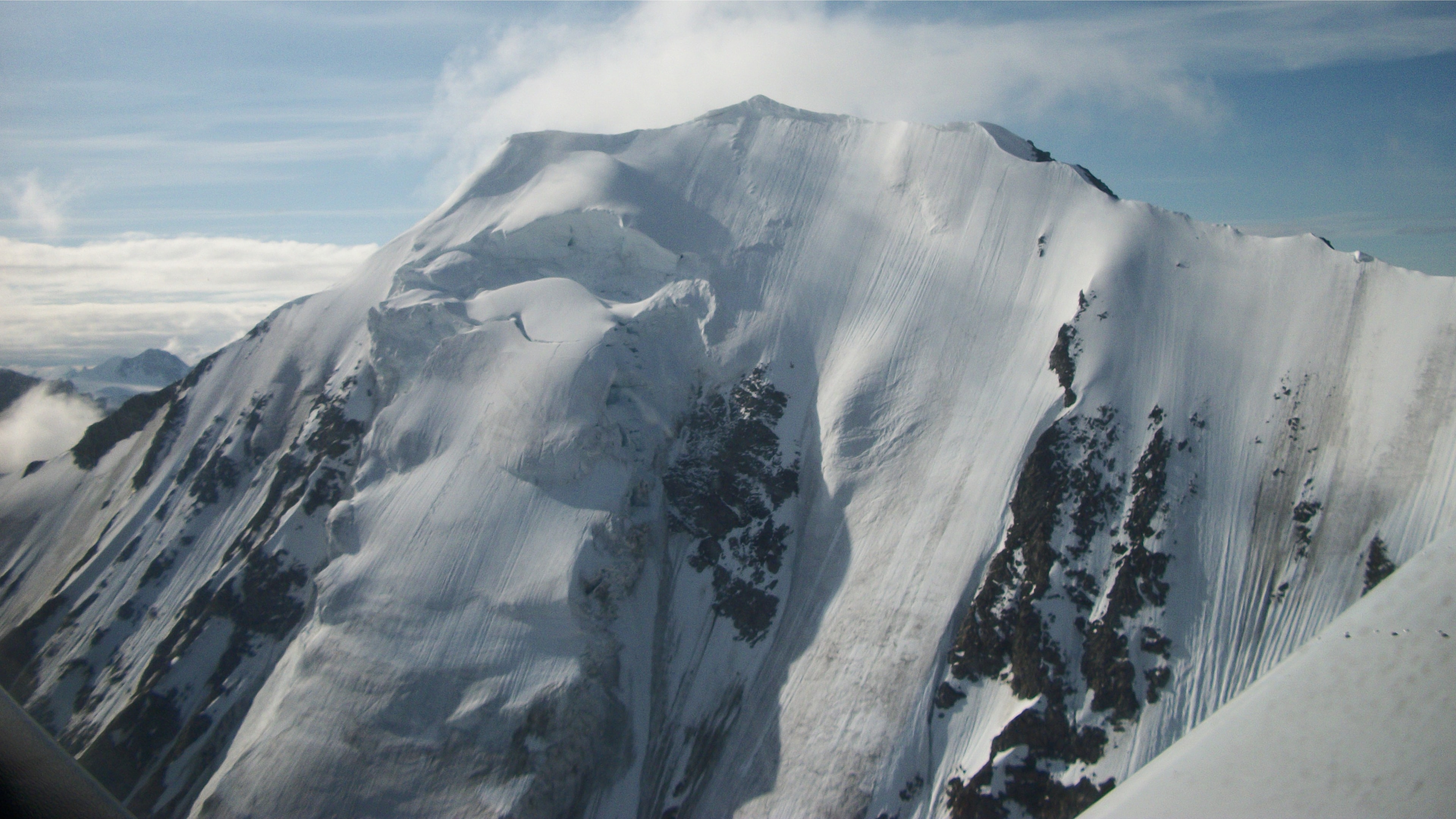 Close aerial view of a massive snow-covered Alaska mountain peak with cloud cap