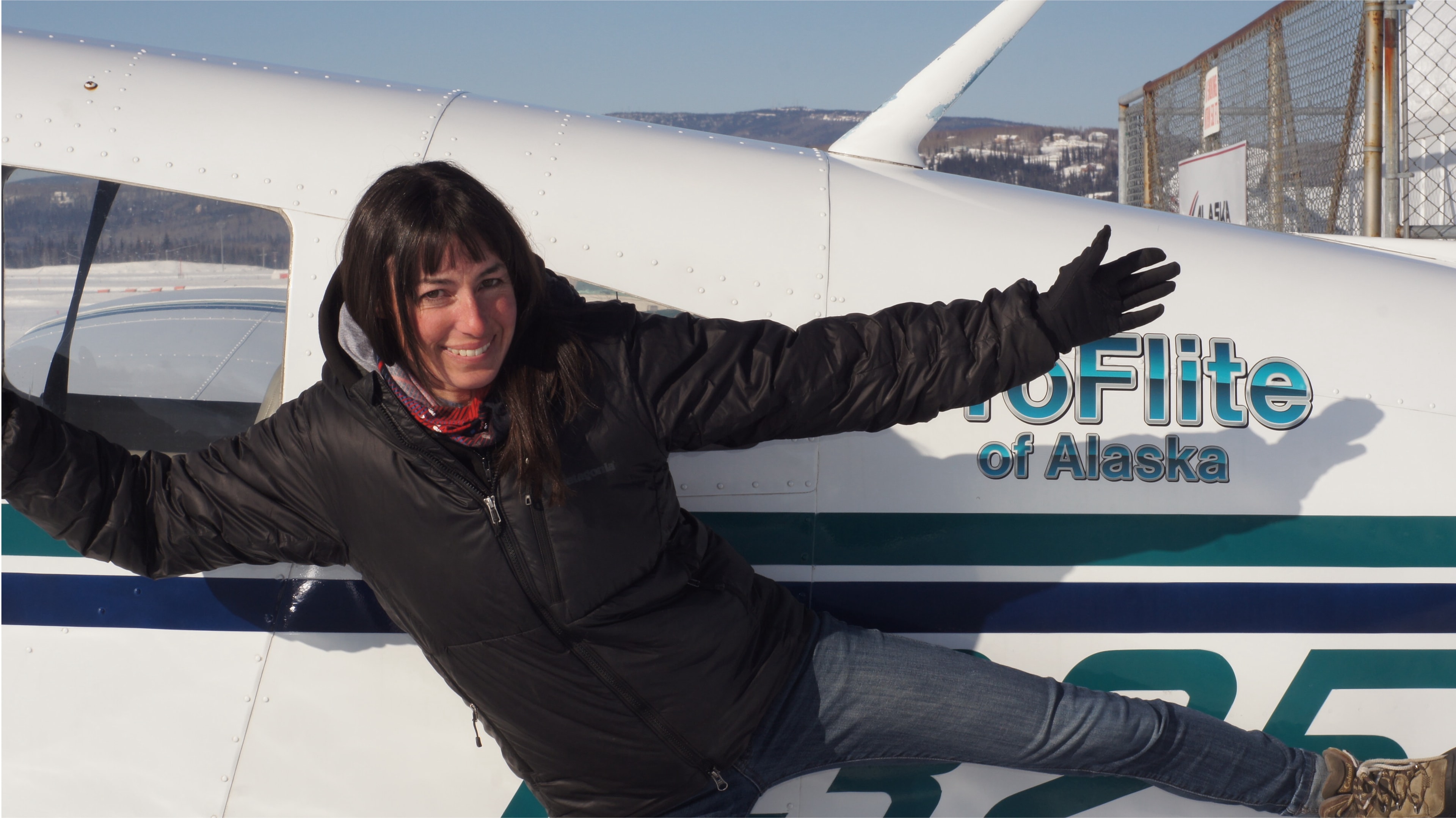 Student posing with arms spread in front of a ProFlite of Alaska aircraft on the ramp
