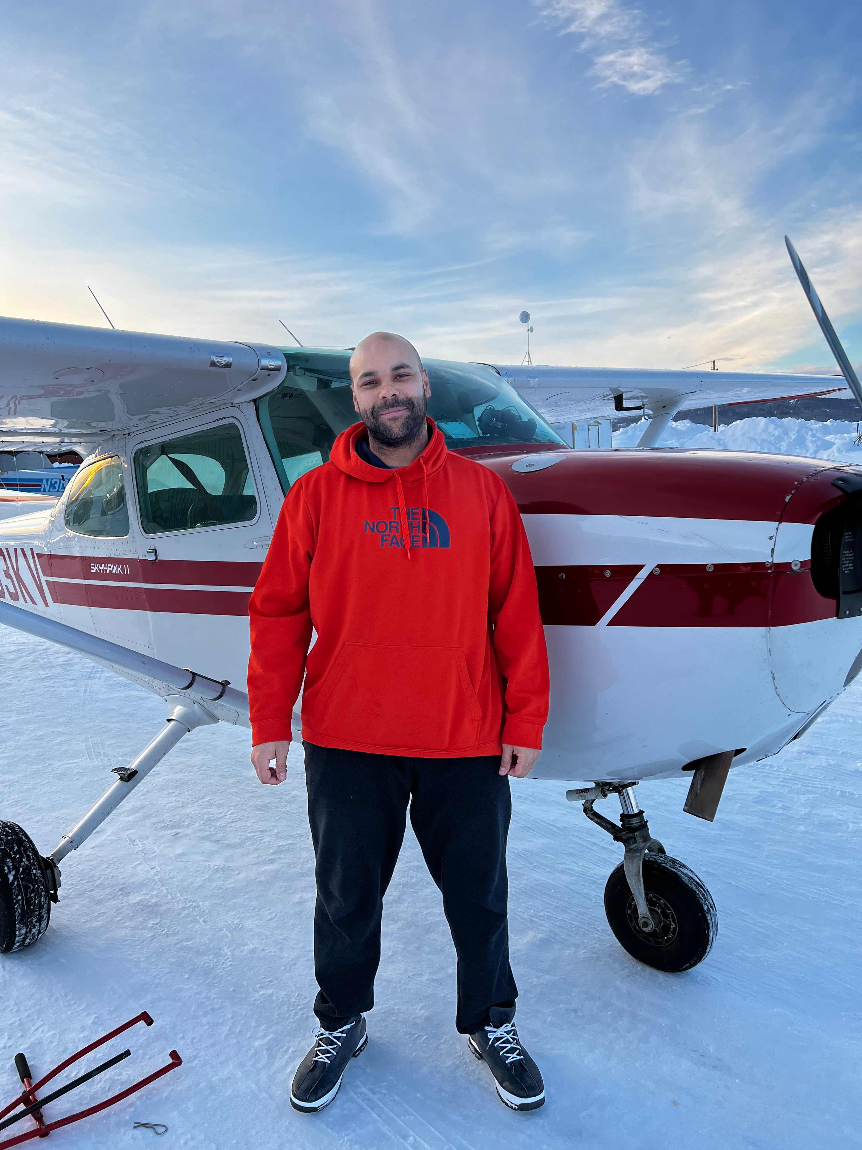 Student in red North Face jacket standing next to a ProFlite Cessna on a snowy Fairbanks ramp