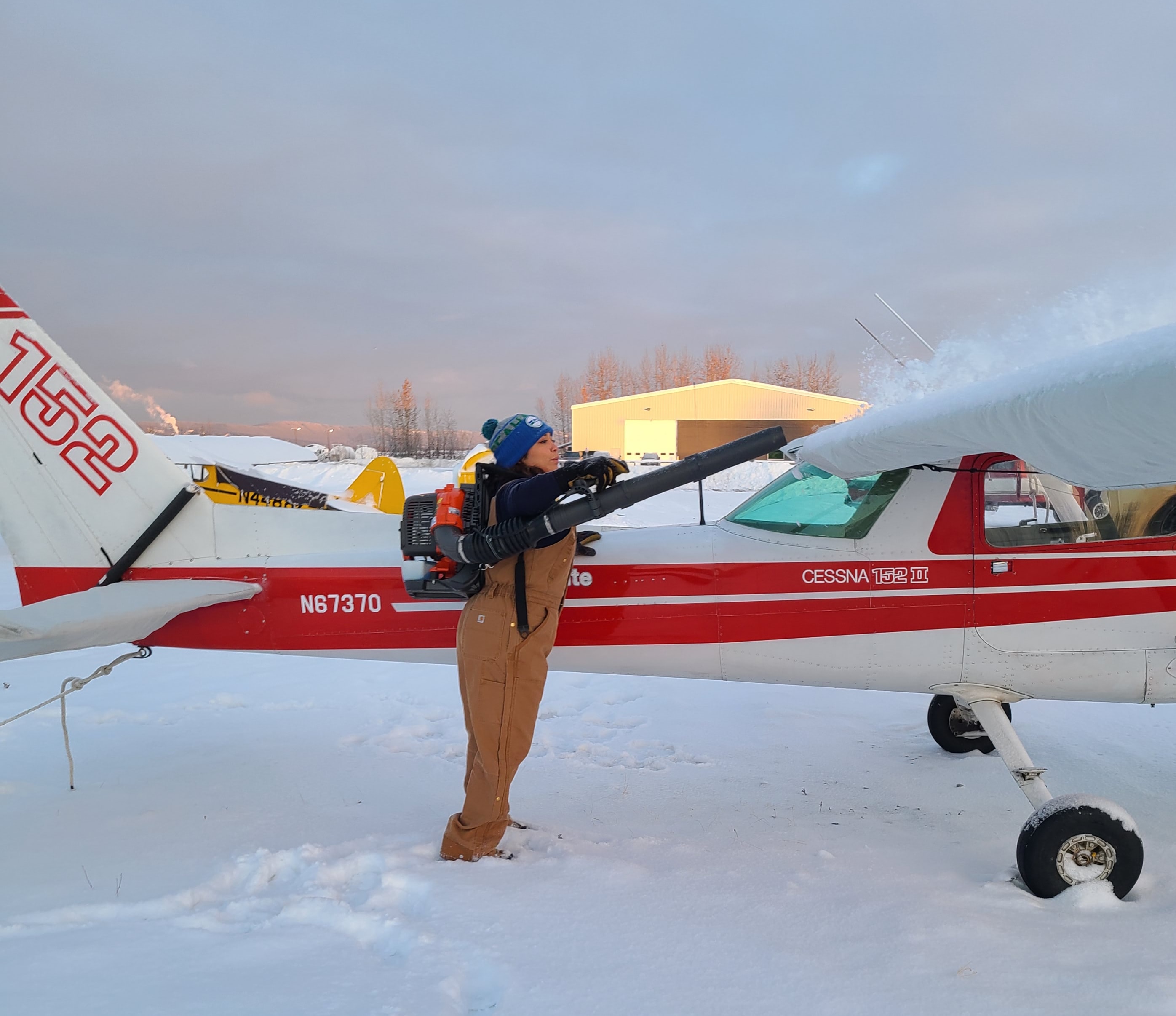 Instructor blowing snow off a ProFlite Cessna 152 N67370 with a backpack blower on a winter morning