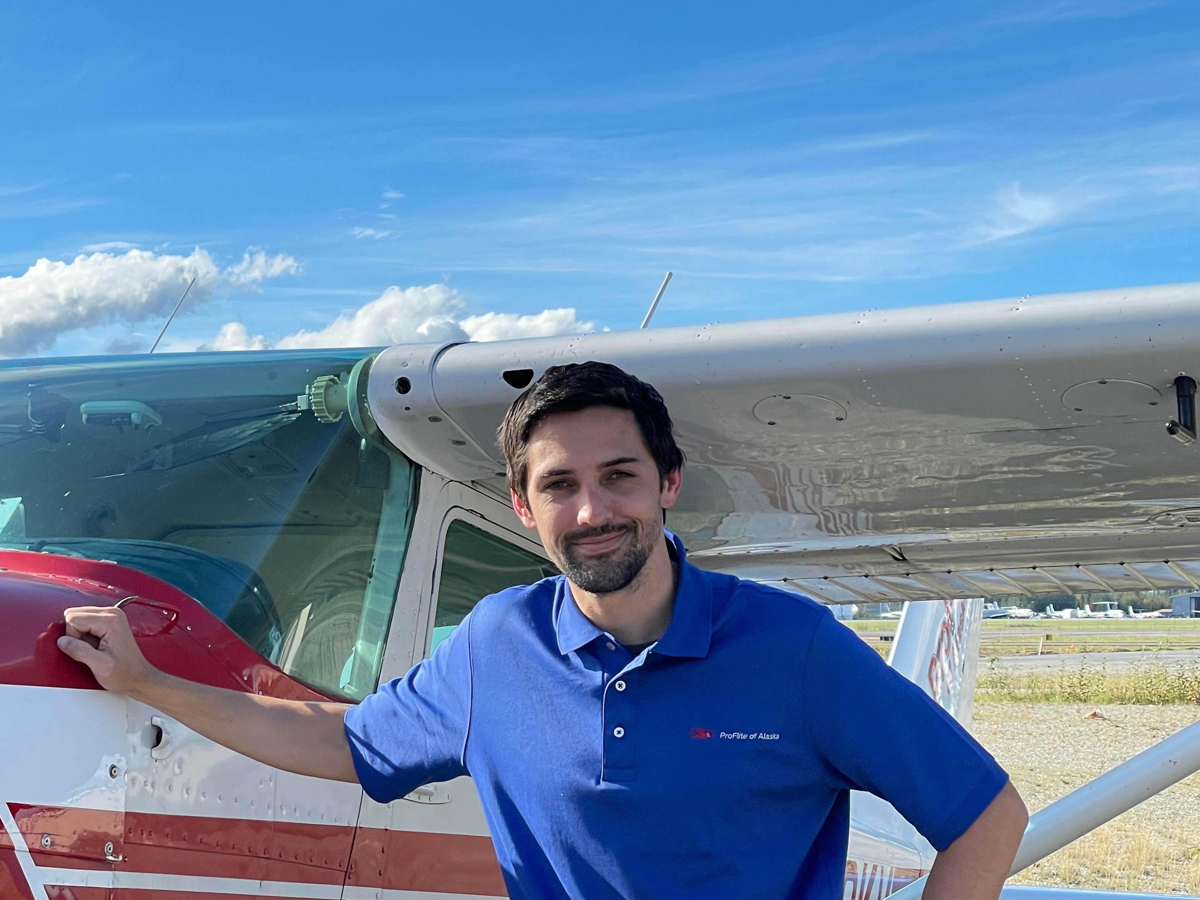 ProFlite of Alaska instructor in blue polo shirt leaning against a Cessna on a clear summer day